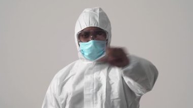 Koruyucu takım elbiseli, maskeli ve kameraya bakan Afro-Amerikan bir adamın portresi. İşaret parmağını sallıyor. Jest yap. Stüdyo, beyaz arkaplanda izole.