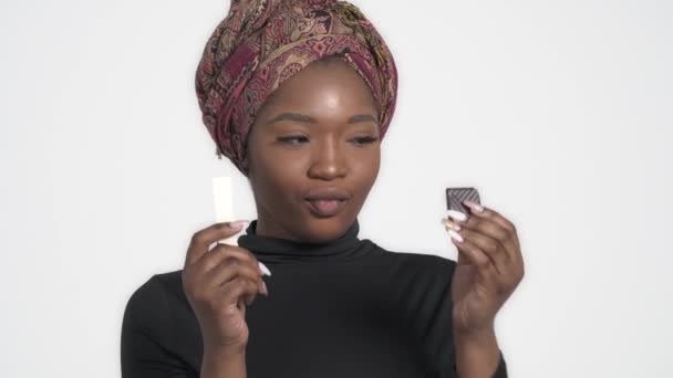 白と黒のチョコレートを選ぶ若い魅力的なアフリカの女性 隔離された白い背景に — ストック動画