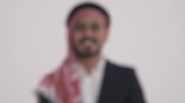 Arap sakallı, kendine güvenen, geleneksel Shemagh 'ta kameraya gülümseyen bir adamın yakın plan portresi. İzole edilmiş, beyaz arka planda. Kamera görüntüsünü değiştirmeye odaklan