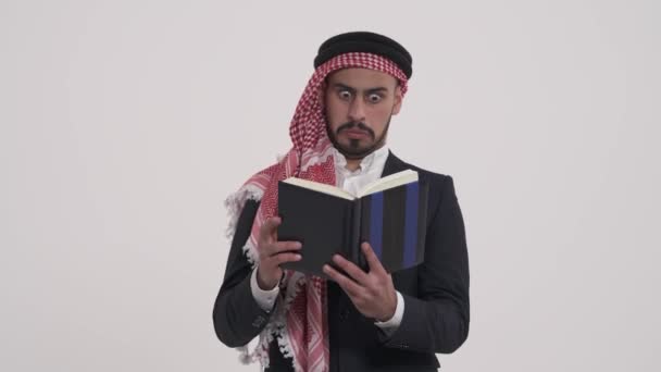 一个疑神疑鬼的阿拉伯人一边看书一边翻页 男性模特儿表现出怀疑的表情 在白色背景下孤立无援 — 图库视频影像