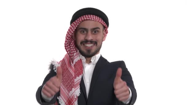 年轻英俊的阿拉伯男子戴着头巾 竖起大拇指表示幸福 被白色隔离 真正的感情身体语言概念 — 图库视频影像