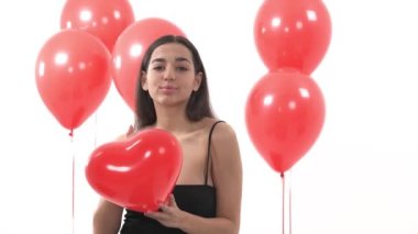 Kalp şeklinde kırmızı balon tutan muhteşem kadın manken hava öpücüğü yolluyor. Bir grup kırmızı yuvarlak balonun yanında duran kadın.