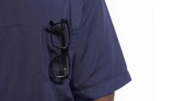 非裔美国医生拿着听诊器 医生穿着蓝色制服 口袋里有眼镜的特写镜头 在白色背景下孤立无援 — 图库视频影像