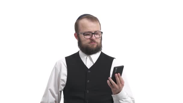 一个拿着智能手机的年轻犹太人的画像 看着屏幕 表达惊讶的情绪 震惊的人使用他的小玩意 在白色背景下孤立无援 — 图库视频影像