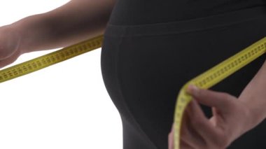 Hamile, beyaz bir kadının karnına yakın çekim. Göbek ölçümü. Ağır çekim. Beyaz arkaplanda izole.