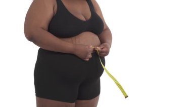 Beyaz arka planda izole edilmiş belini ölçen iç çamaşırlı, tanınmayan siyah ve iri bedenli bir kadının yakın çekimi.