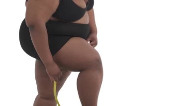 Beyaz arka planda izole edilmiş kalçasını ölçen iç çamaşırlı Afro-Amerikan obez kadının yakın çekimi.