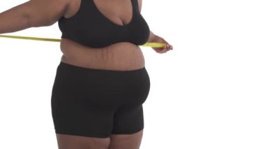 Beyaz arka planda göğüs ölçüsünü ölçen iç çamaşırlı, tanınamayan Afrikalı obez kadının yakın plan fotoğrafı.