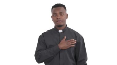 Yakışıklı Afrikalı rahibin portresi göğsünü elle okşuyor. Beyaz arka planda izole edilmiş saygı ve takdiri ifade eden bir şeyler söylüyor.