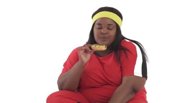 非洲肥胖妇女穿着运动服吃甜甜圈的特写 与白人背景隔离 — 图库视频影像