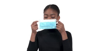 Siyah yakalı polo giyen genç bir Afrikalı kadın kendini ve diğer insanları korumak için maske takıyor. Beyaz arkaplanda izole edilmiş.