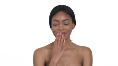 Çıplak omuzlu, dudaklarını elleriyle kapatan, gülümseyen ve kameraya poz veren baştan çıkarıcı Afrikalı kadın. İzole edilmiş, beyaz arkaplanda