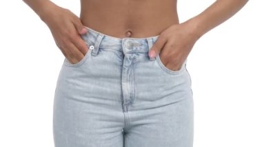 Tanınamayacak kadar ince, dar Afrikalı bir kadının mavi dar kotunun cebine elini koymasının ön görüntüsü. İzole edilmiş, beyaz arkaplanda