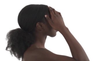 Beyaz arka planda genç Afrikalı bir kadının profili. Tek eliyle yüzünü okşuyor ve yavaşça kameraya doğru dönüyor.