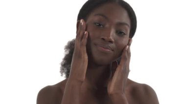 Beyaz arka planda, yüzüne hafifçe dokunan genç siyahi kadının yakın plan portresi.