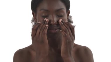 Genç siyahi bir kadının portresi beyaz arka planda parmaklarıyla yüzüne masaj yapıyor.