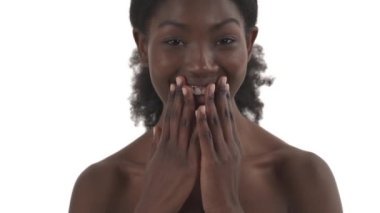 Genç Afrikalı bir kadının tam yüz portresi. Neşeli, sürpriz bir ruh hali içinde. Ağzını kapatıyor, gülümsüyor ve ellerini beyaz arka planda çırpıyor.