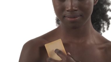 Genç Afrikalı bir kadının portresi omuzlarını ve yakasını banyo süngeriyle okşuyor ve beyaz arka planda dönüp duruyor.
