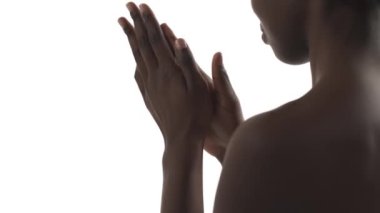 Beyaz arka planda ellerine krem süren Afrikalı genç bir kadının görüntüsü.