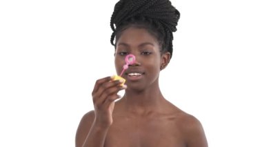 Afro örgülü genç Afrikalı bir kızın portresi kameraya sabun köpüğü üflüyor ve beyaz arka planda izole bir şekilde gülümsüyor.