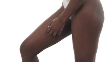 İç çamaşırlı, bacaklarını tırmalayan Afro-Amerikan sıska bir kızın yan görüntüsü. Sağlık sigortası konsepti. Beyaz arkaplanda izole