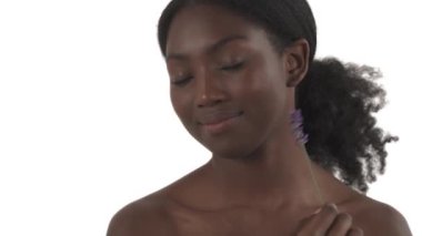 Genç siyah gülümseyen kadının yakın plan portresi yüzünü lavanta dalıyla okşuyor ve beyaz arka plandaki kameraya bakıyor.