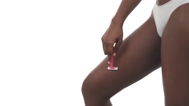 コピースペースとスリムなアフリカの少女の足の側面 安全剃刀で太ももを剃る若い女性 白地に隔離された — ストック動画
