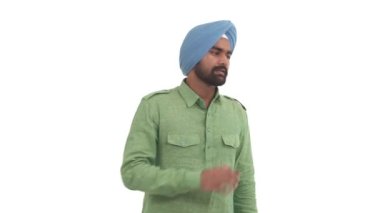 Sakallı genç Hintli adam konuşuyor ve yan bakıyor, ağzının yanında el ele tutuşuyor. Beyaz arkaplanda izole