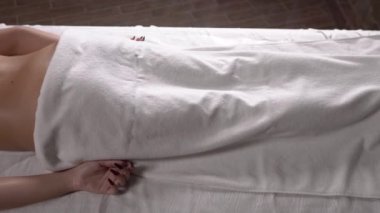 Lüks kaplıca kulübünde sırt masajı yapan sofistike bir masörün soldan sağa vuruşu. Vücut bakımı konsepti. Genç ve çekici bir kadın masaj masasında yatıyor.