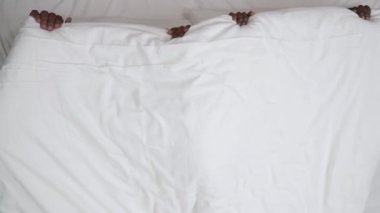 Battaniyenin altına gizlenmiş siyah çiftin üst görüntüsü. Aniden atarlar ve yataktan atlarlar. Çünkü sevgililer uyuyakalır.