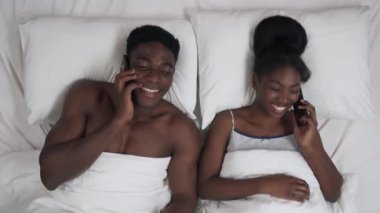 Afro-Amerikalı çiftin yatakta uzanmış cep telefonlarıyla konuşmalarının en üst görüntüsü..