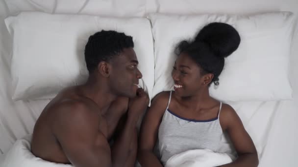 若いアフリカのカップルのトップビューのベッドに横たわっている 男は彼のガールフレンド面白い話をし 彼女の鼻に触れ 顔を作る 笑う恋人 — ストック動画