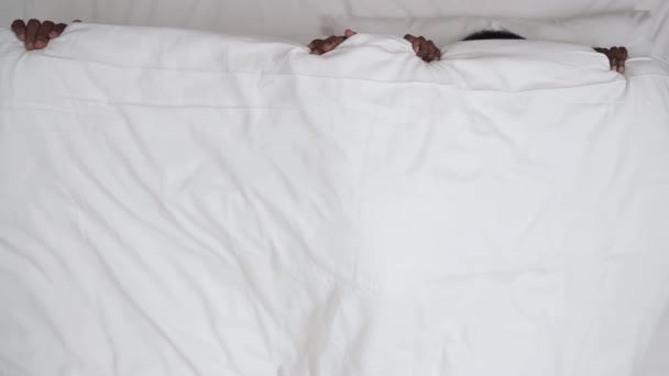 毛布で覆われたベッドに横たわっアフリカのカップルのトップビュー それを引っ張っと広い目でお互いでゴボゴボ — ストック動画
