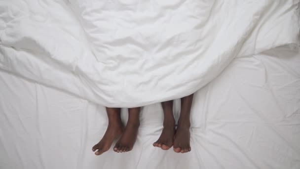 白い毛布の下に横たわって黒のカップルの揺れるダンスの足の上のビュー 愛と家族の概念 — ストック動画