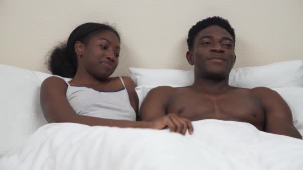 アフリカ系アメリカ人のカップルの肖像画のベッドに横たわっている 毛布を持ち上げ男の陰茎勃起のために驚きを表現する女性 性生活の概念 — ストック動画