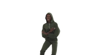 Kapüşonlu eşofman giyen Afrikalı kadın afro tarzı dans ediyor. Dansçı yan yana adım atıyor, ayaklarını sürüyor, dizlerini itiyor, el kaldırıyor. Beyaz arkaplanda izole.