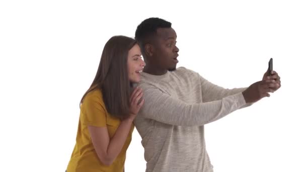 年轻的跨种族夫妇拿着智能手机自拍 摆姿势拍照 展示V标志和鸭脸 因白人背景而被隔离 — 图库视频影像