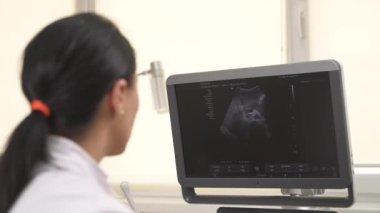 Ultrason muayenesi yaparken tıbbi cihazın monitörüne bakan profesyonel bir kadın doktorun yakın çekimi. Sağlık hizmetleri kavramı