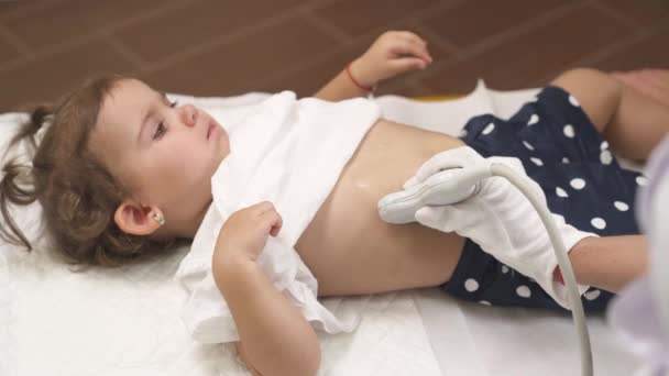 一个儿科医师对她的病人进行超声腹部检查的头像 可爱的小女孩躺在一张白纸上 仰视着医生 — 图库视频影像