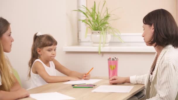 儿童心理学家与两个小女孩一起工作 孩子们用彩色铅笔画画 快乐的年轻治疗师运用图解技巧 — 图库视频影像