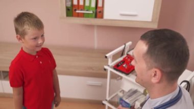 Dost canlısı bir çocuk doktorunun neşeli küçük hastasıyla beşli jestini yüksek açıdan izlemesi...