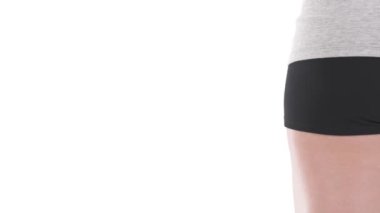 Beyaz kadın sporcunun alt gövdesinin arka görünüşü. Çerçevede topla el beliriyor. Beyaz arkaplanda izole