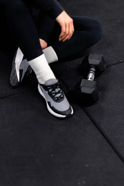 訓練中に再充電し訓練設備の黒い床に座って床にダンベルを付けて 黒のトレーニングパンツ 長い白い靴下 — ストック写真