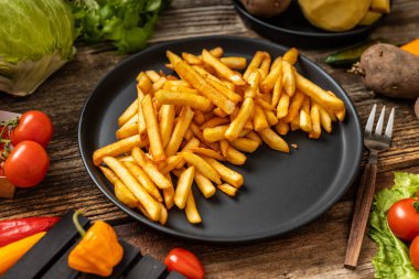 Siyah tabakta servis edilen patates kızartmaları bir sürü sebze ve taze Persley baharatı, ahşap masa, ahşap saplı çatal.