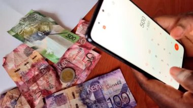 Akıllı telefon hesap makinesi kullanarak finans hesaplayan kadın eller. Sade. Kenya banknotları masanın üzerinde. Bütçe, planlama konsepti.