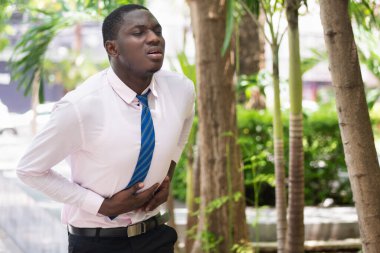 Karnı ağrıyan Afrikalı bir adam, ofis sendromu, karın ağrısı, ishal, kabızlık, mide iltihabı, mide reflüsü, mide kanseri olan çok çalışan Afrikalı bir ofis çalışanı.