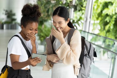 Asyalı ve Afrikalı üniversite öğrencisi bilgisayar tabletine bakıyor ve birlikte gülüyorlar, uluslararası öğrencilerle okul konseptine geri dönmekten mutlular.