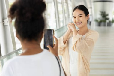 African woman taking live streaming video for her asian Chinese friend clipart