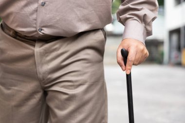 Hand closeup of overweighted senior old man with bad knee joint, walking with walking aid stick clipart