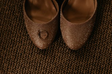 Yüksek topuklu kadın yüzüğüyle. Gelinin sabahı. Kadın ayakkabılarının arasına elmas ve mücevher takılmış nişan yüzüğü. Parlak sandaletler koyu bej bir halıda duruyor.